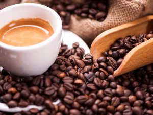 scoop of coffee beans surrounding a cup of espresso