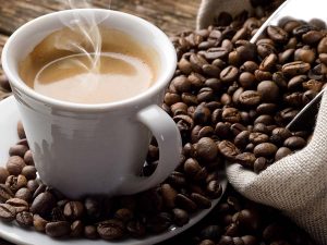 white coffee cup on saucer surrounded by a spilt bag of coffee beans