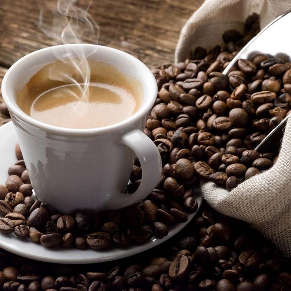 white coffee cup on saucer surrounded by a spilt bag of coffee beans